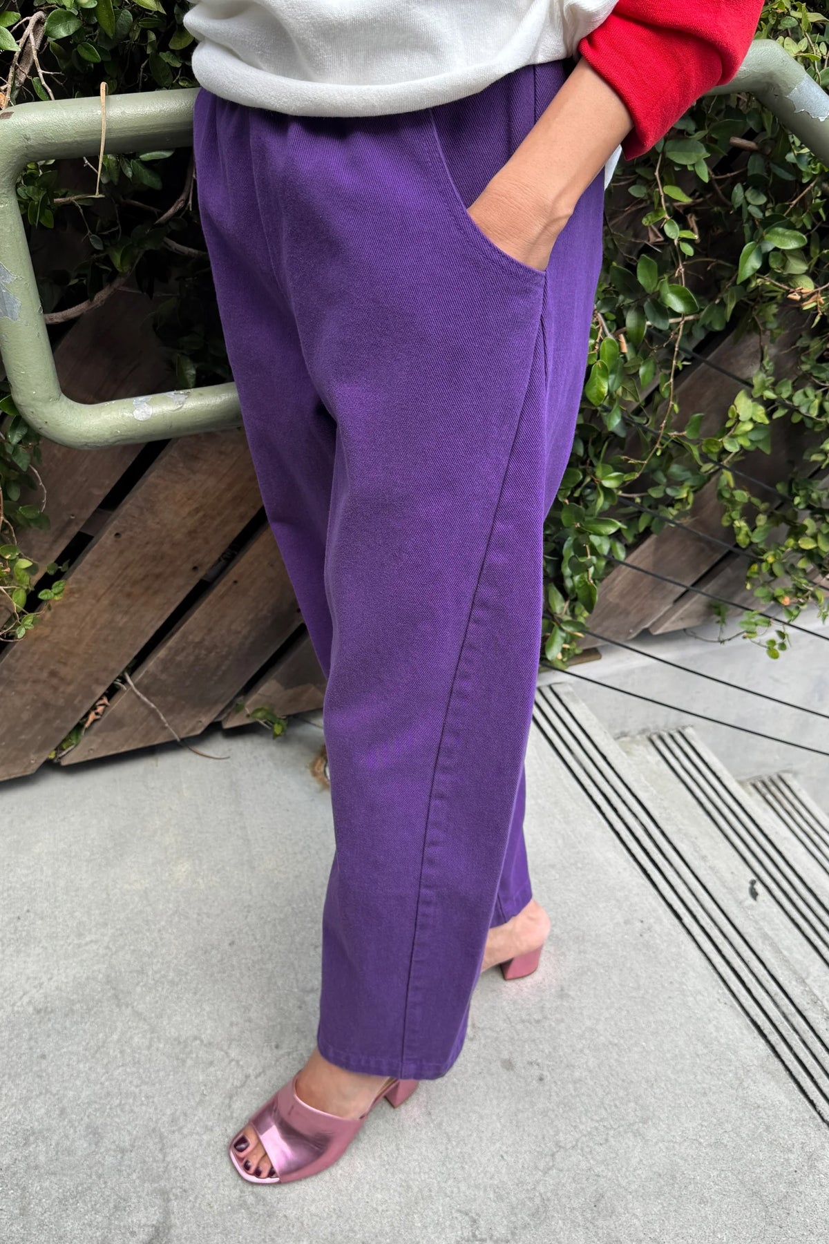 Eggplant purple Arc Pants, side view showing pocket and leg seams, worn with pink heeled sandals.
