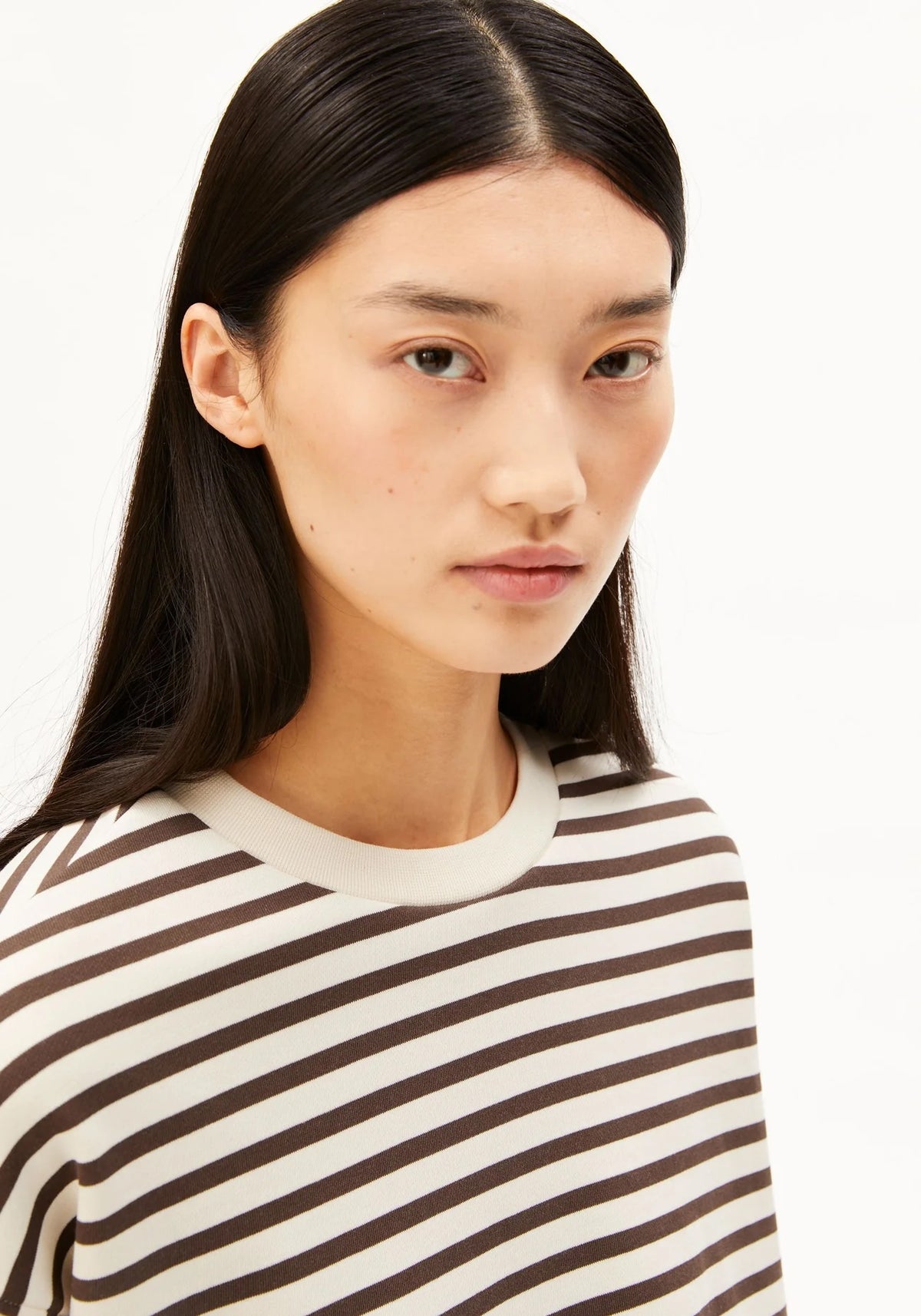 A close-up shot of a model wearing a brown and cream striped crewneck top against a plain white background.