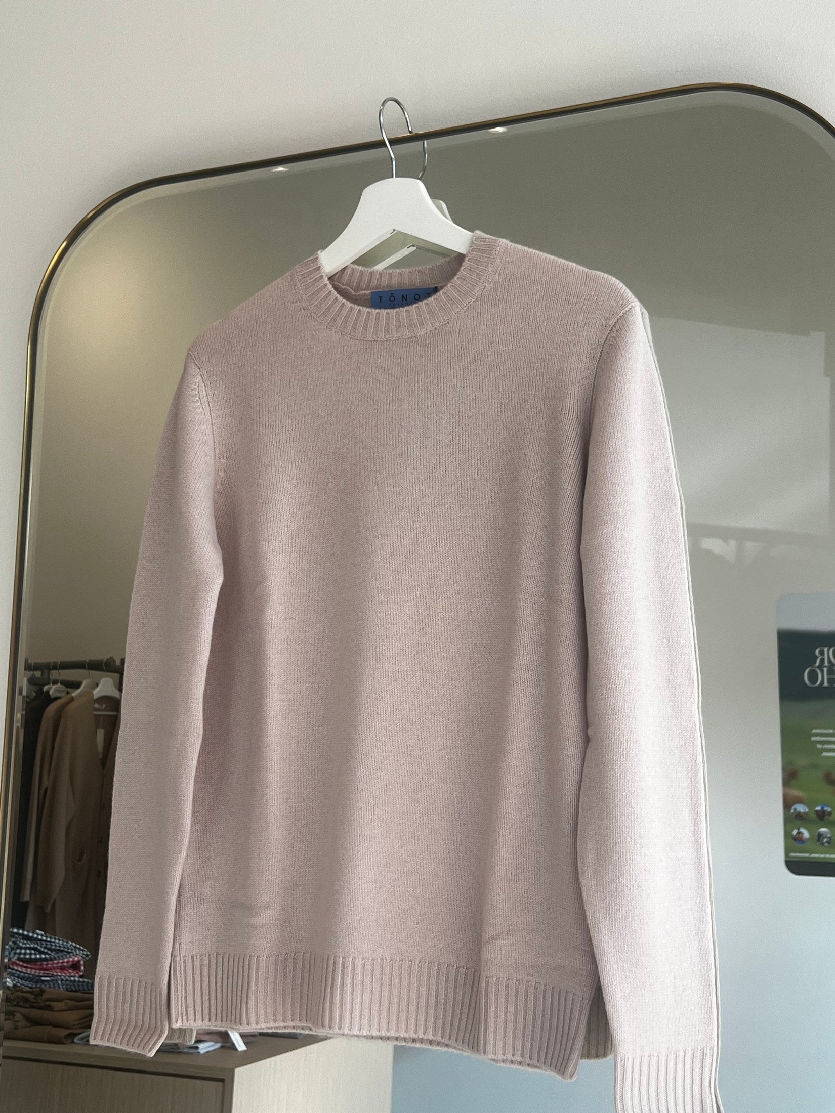 Soft beige round neck cashmere sweater hanging on white hanger in a modern room setting