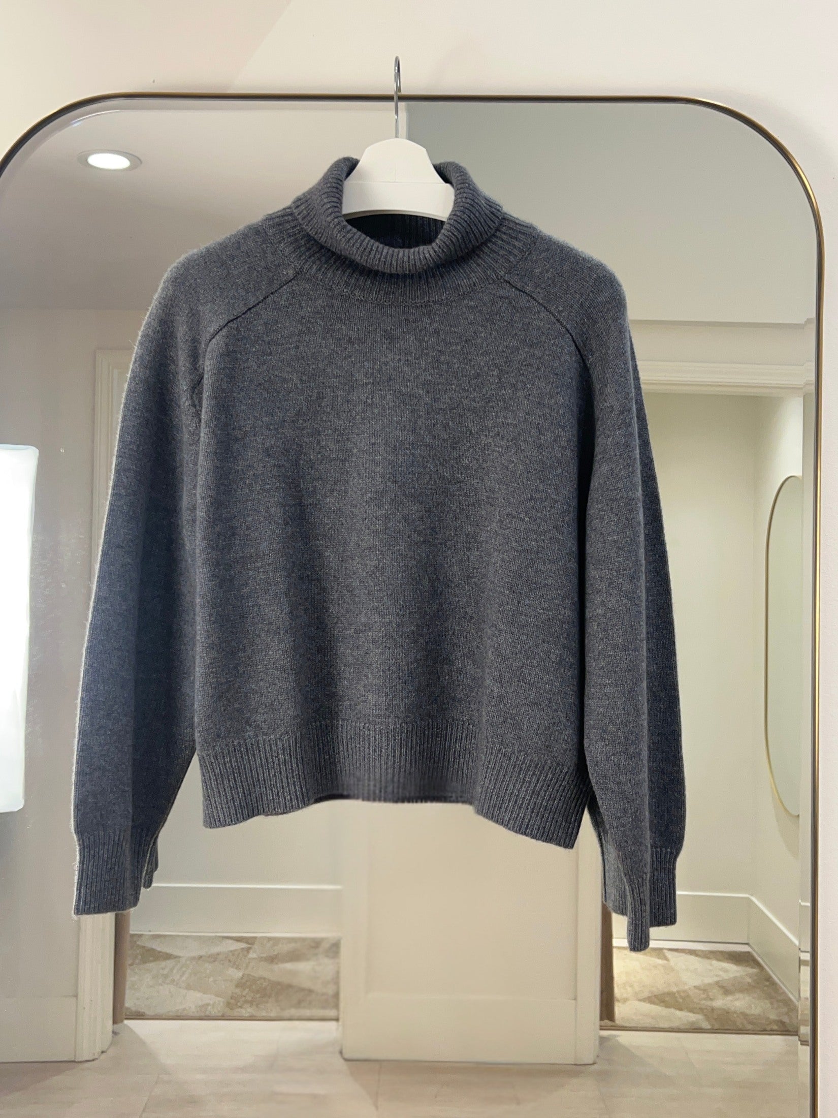 Grey turtle neck cashmere sweater with raglan shoulders hanging on white hanger against mirror background