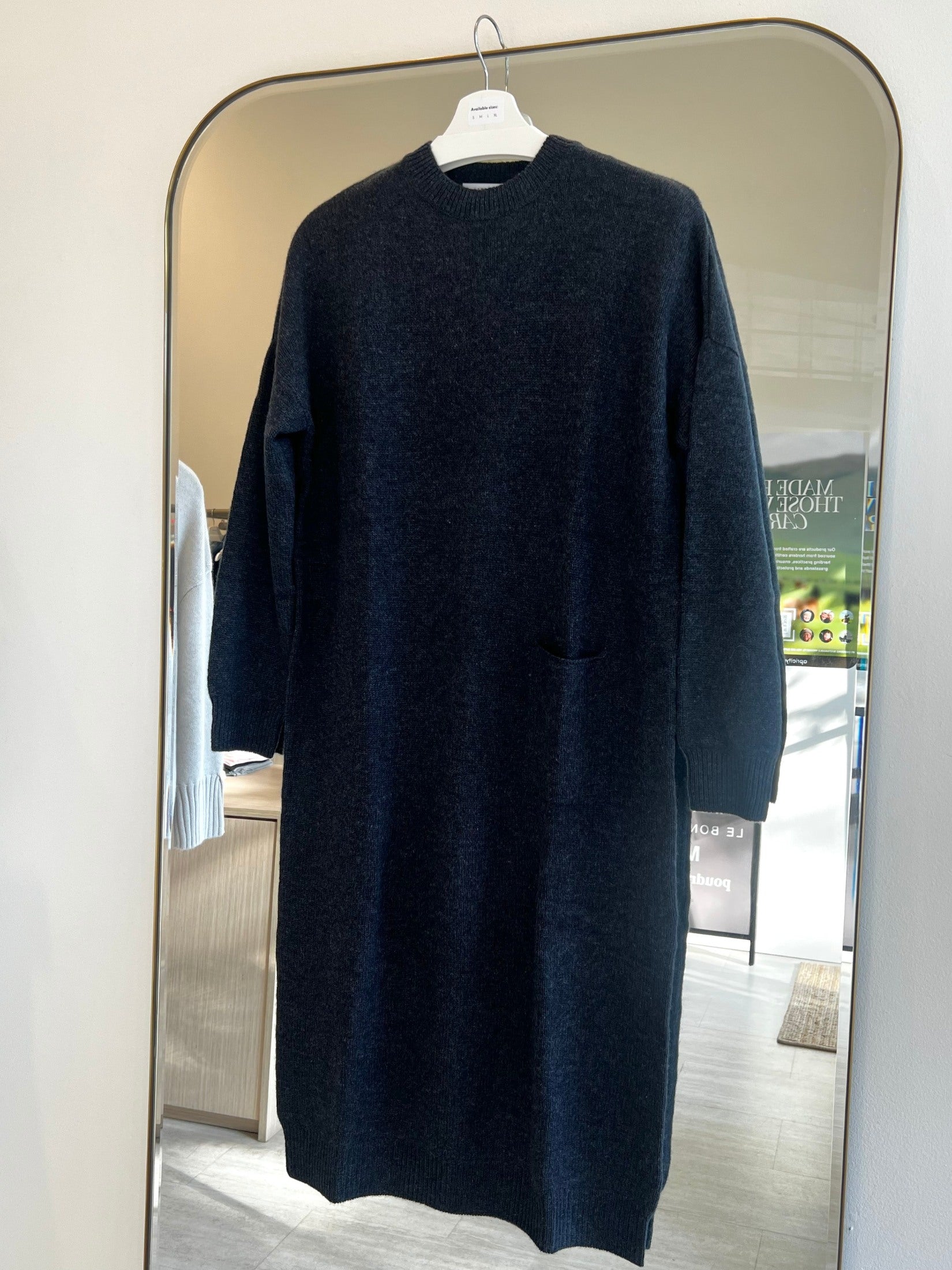 Relaxed fit black cashmere dress with round neck and one pocket hanging on a hanger in front of a mirror