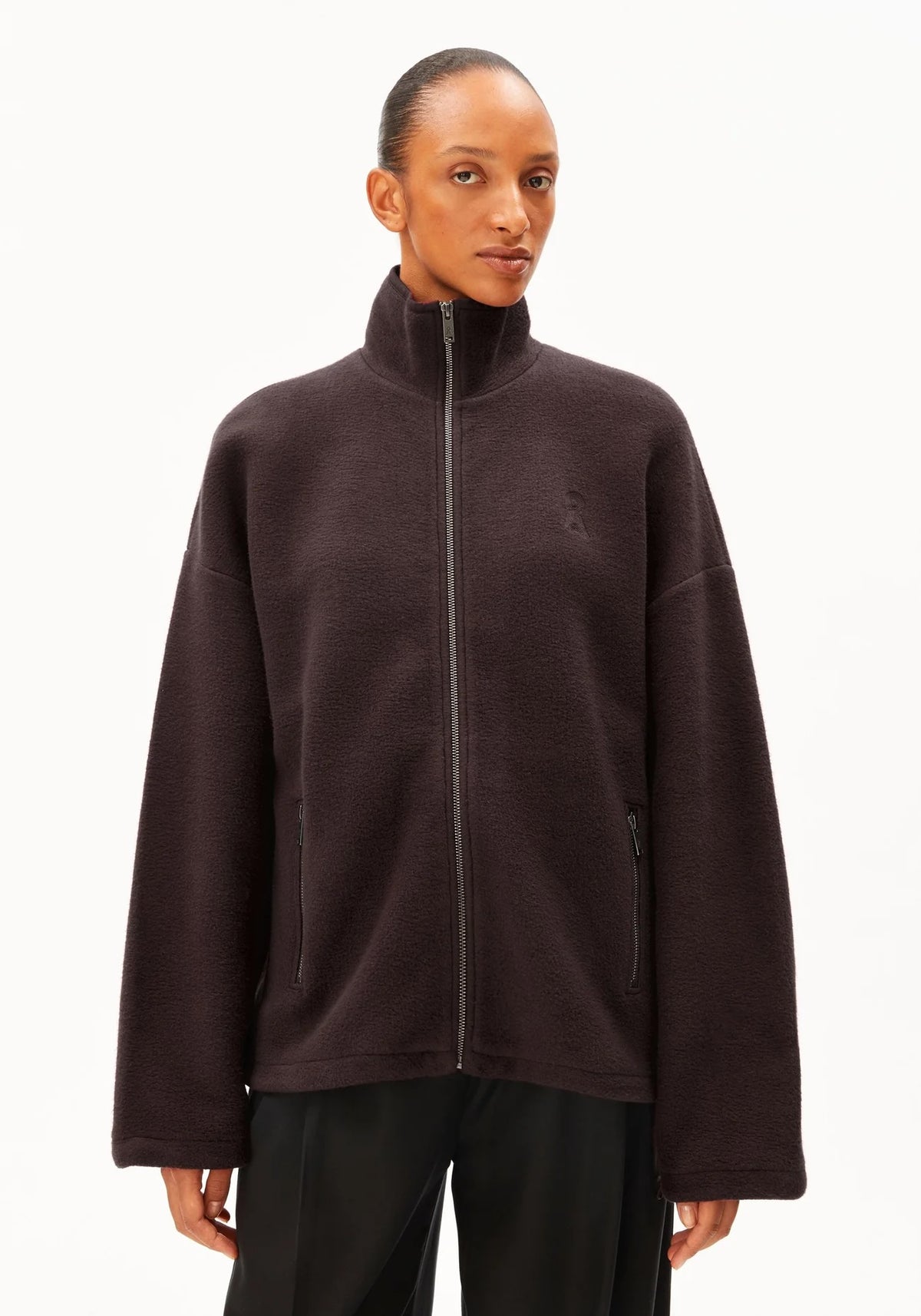 A model wearing a dark brown fleece zip-up jacket with a high collar and black pants, photographed against a clean white background.
