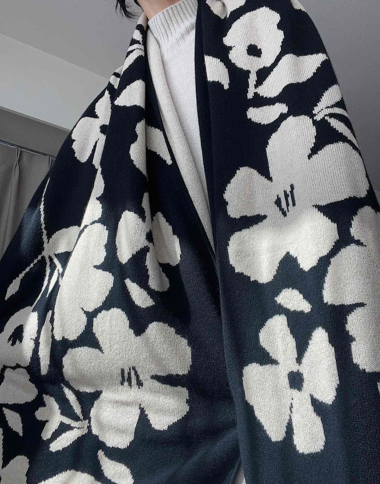 A black and beige floral cashmere scarf, delicately draped to showcase its soft texture and elegant pattern.