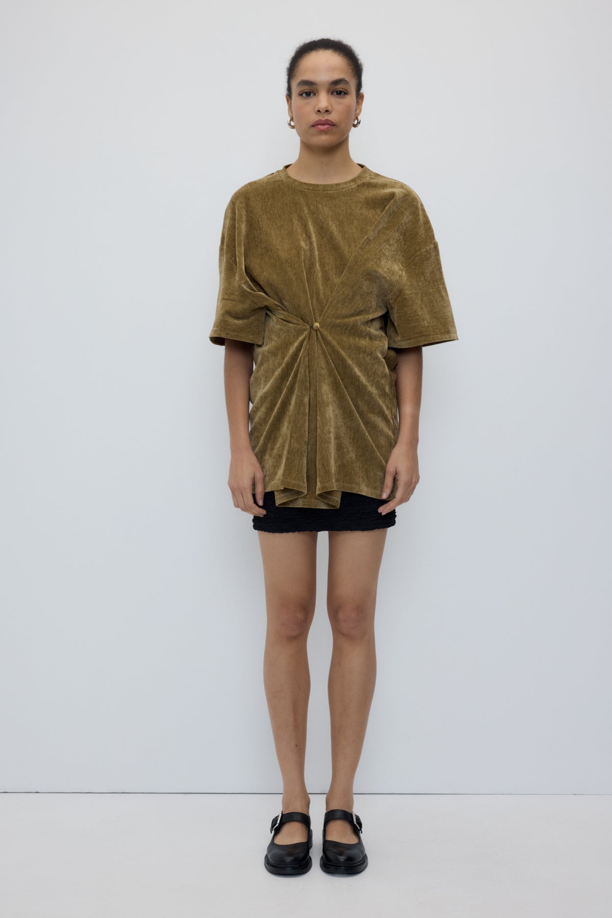 Woman wearing a green velvet top and black shorts against a white background