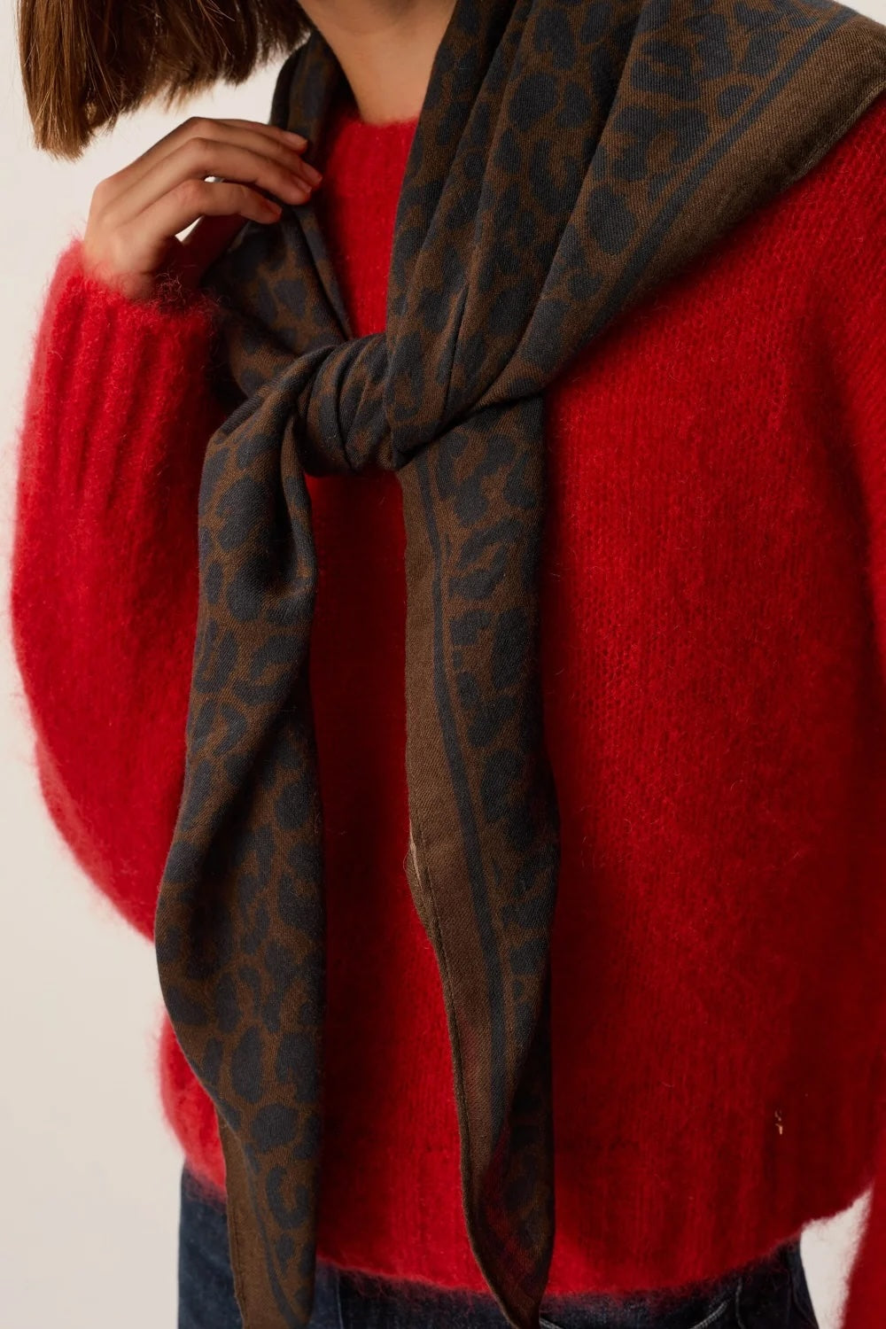 A close-up of a person wearing a bright red fuzzy sweater and a dark brown scarf with a leopard print pattern, tied around the neck.