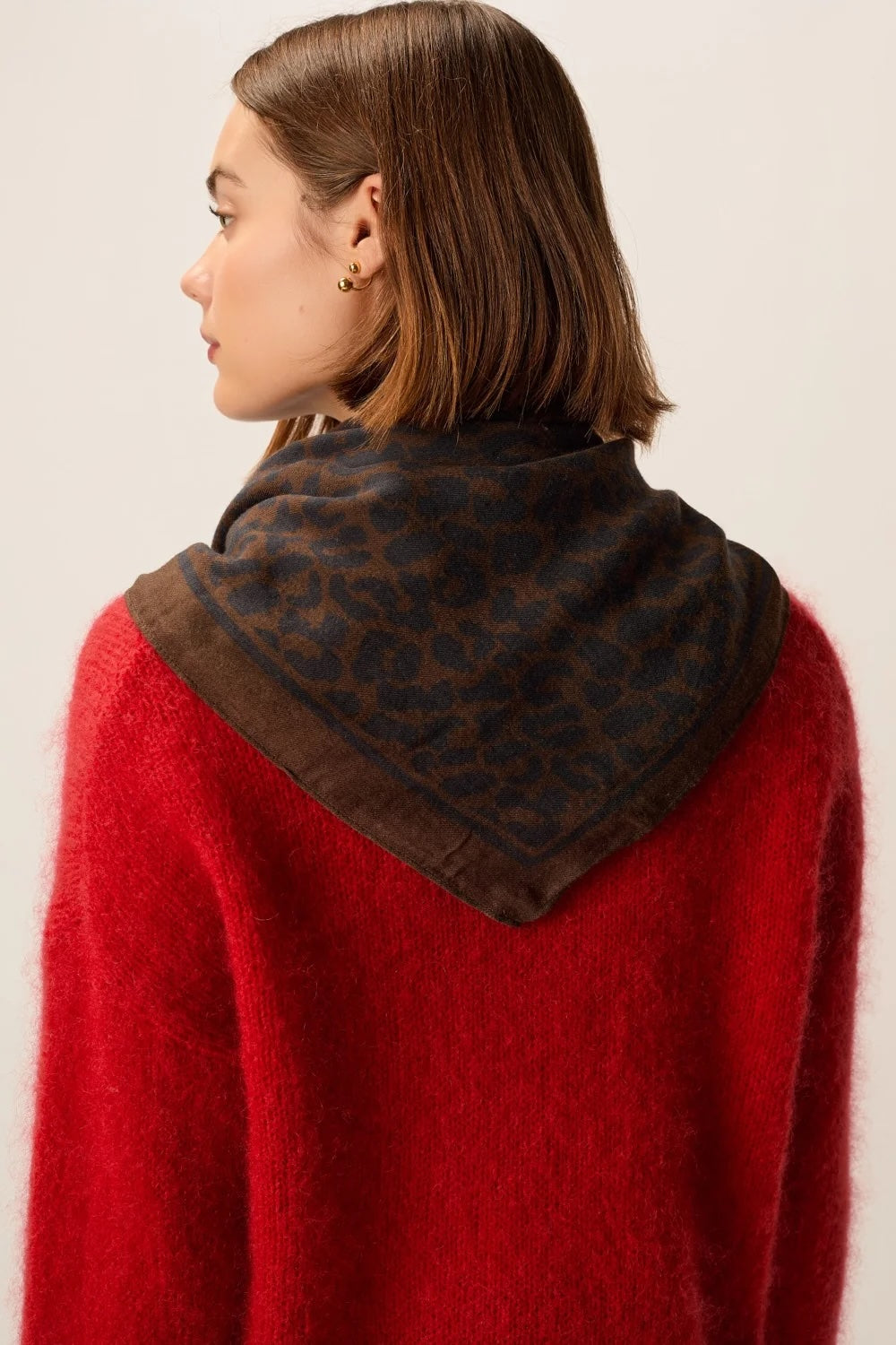 A woman shown from the back wearing a bright red fuzzy knit sweater and a dark brown leopard-print scarf with a solid brown border.