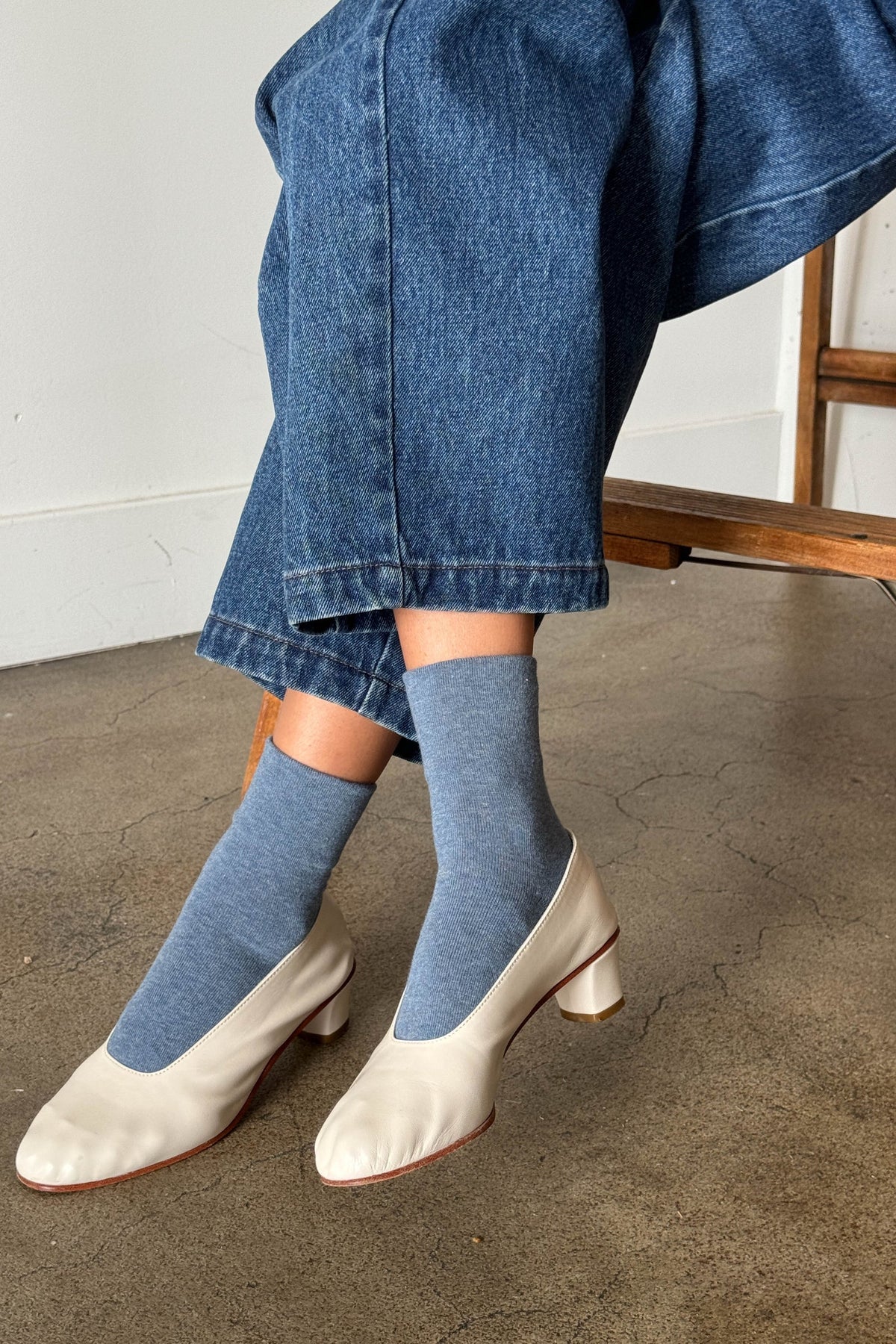 Person wearing blue socks and white shoes with a denim skirt.
