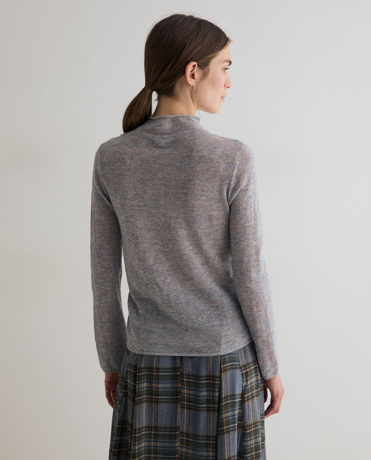 A woman shown from the back wearing a heather gray mock neck long-sleeve knit sweater and a blue-gray plaid skirt, set against a plain light gray studio background.