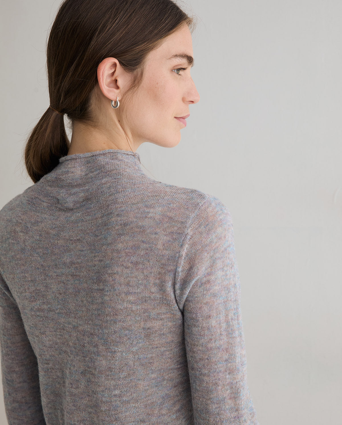 A woman shown from the back and side profile wearing a heathered gray knit mock-neck sweater against a plain light gray background.