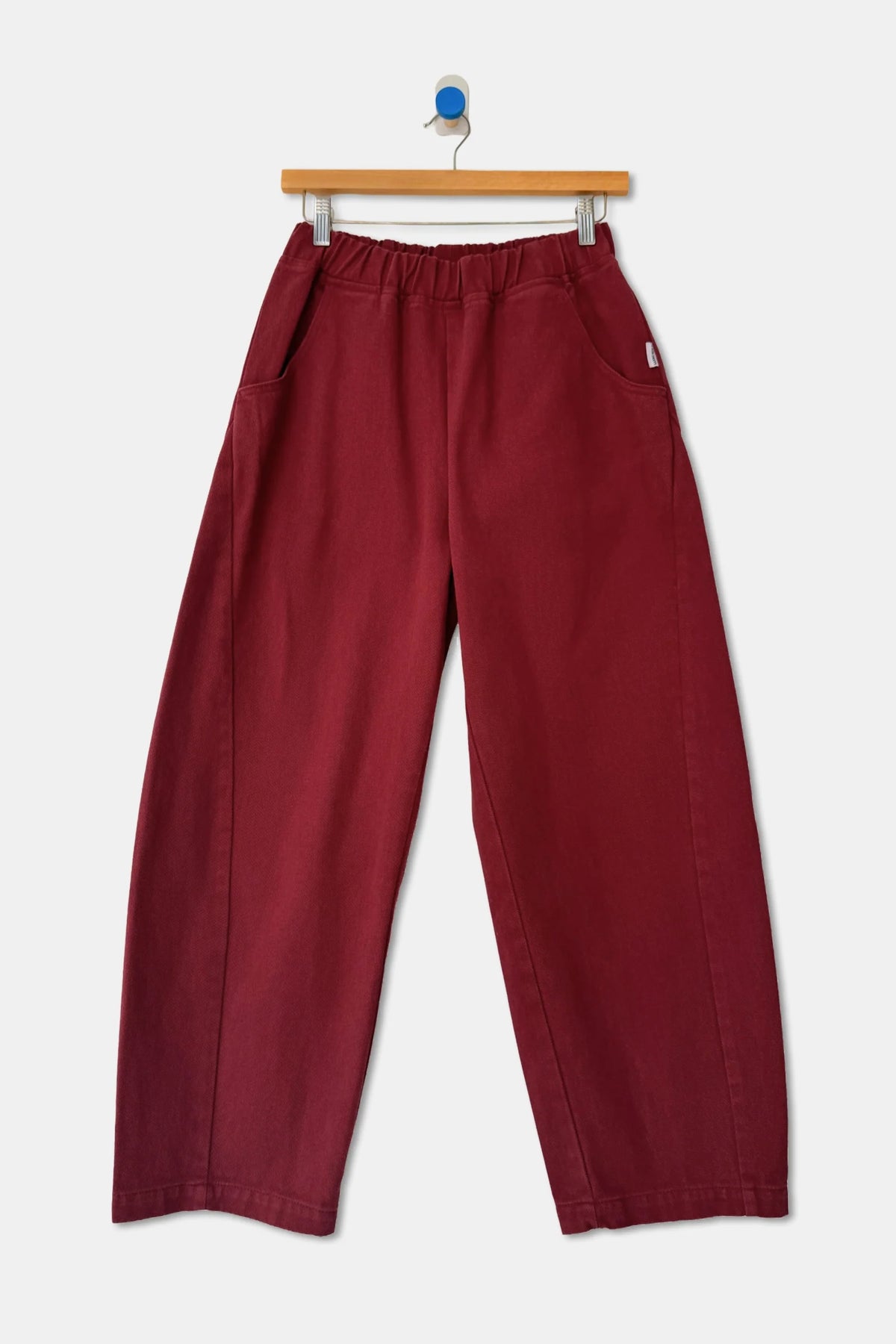 Oxblood Arc Pants on a hanger, front view showing elastic waistband, pockets and barrel-shaped legs