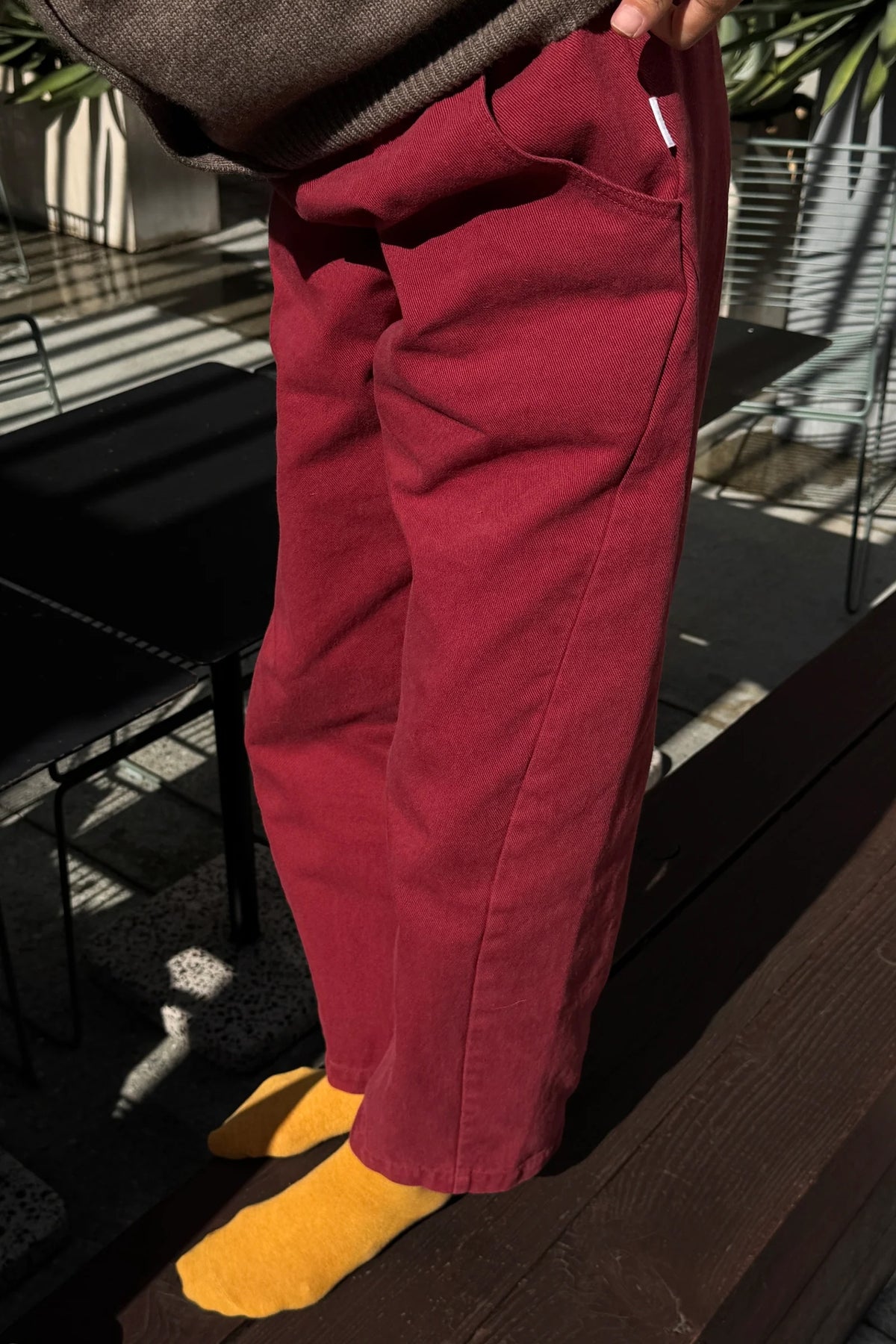 Oxblood Arc Pants, angled view showing pocket, textured fabric and cropped hems, worn with yellow socks