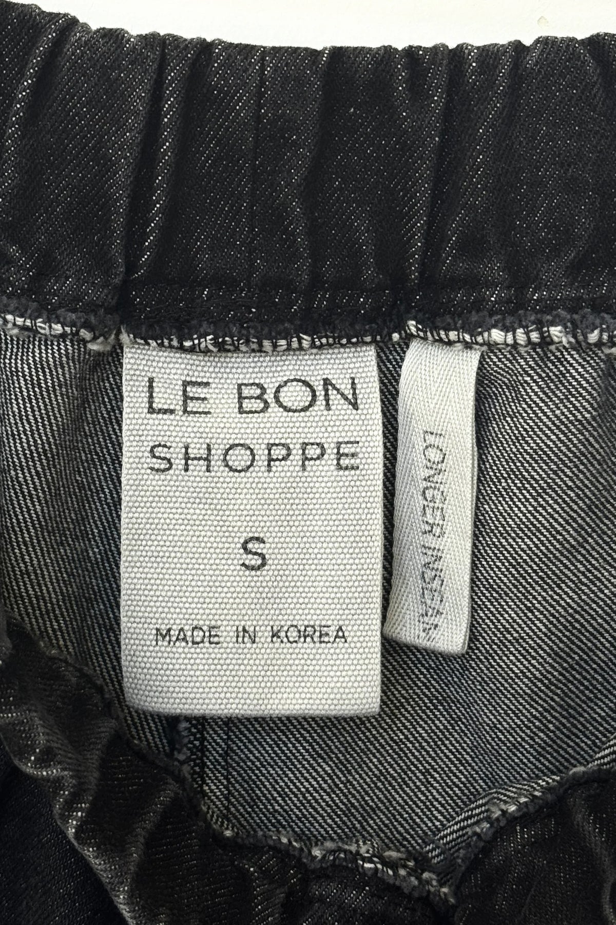 Close-up of the inside waistband of black denim jeans, showing a white fabric label that reads 'LE BON SHOPPE', size 'S', and 'MADE IN KOREA', alongside a side tag reading 'LONGER inseam.