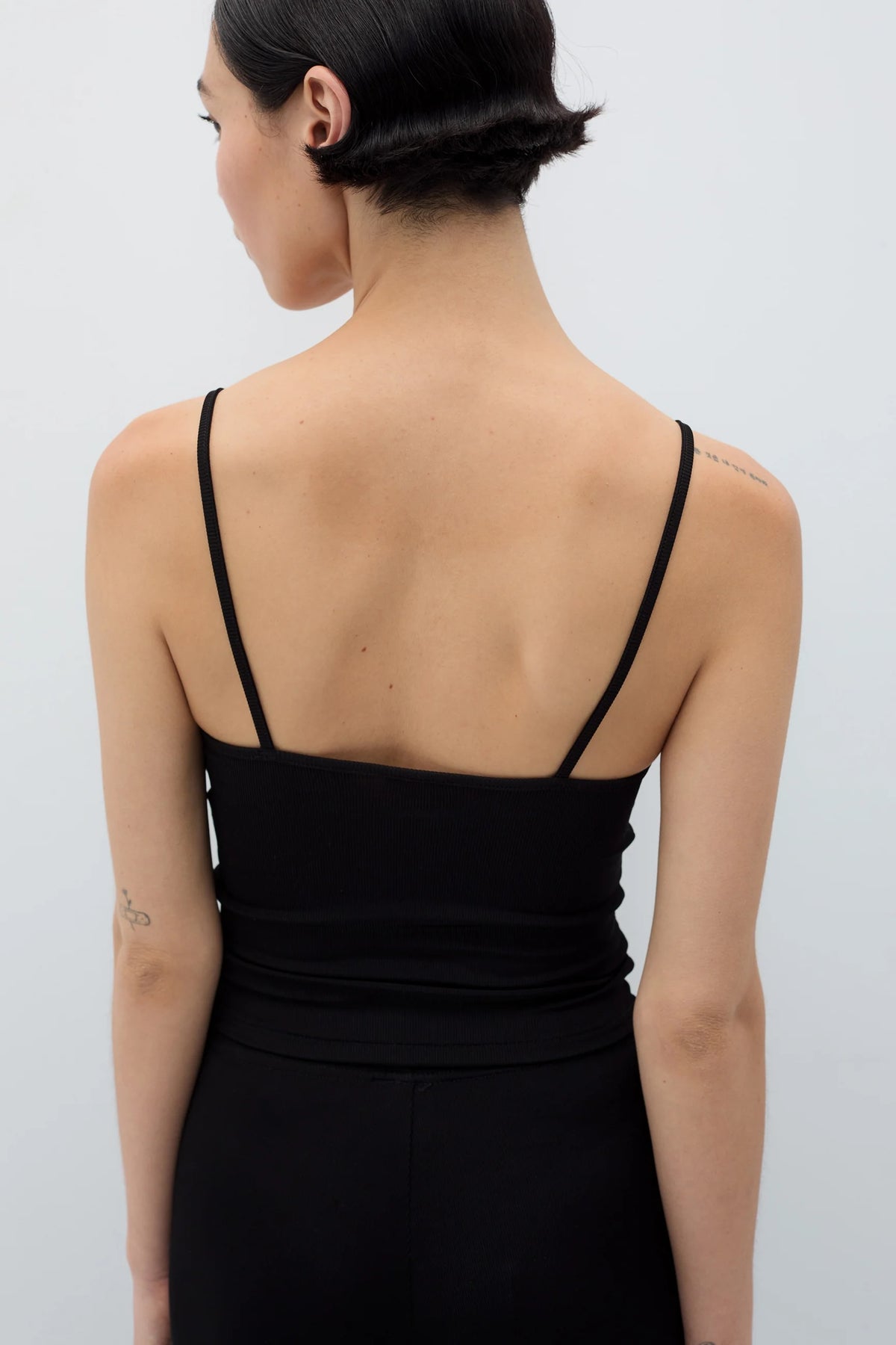 Person wearing a black dress with thin straps on a plain background
