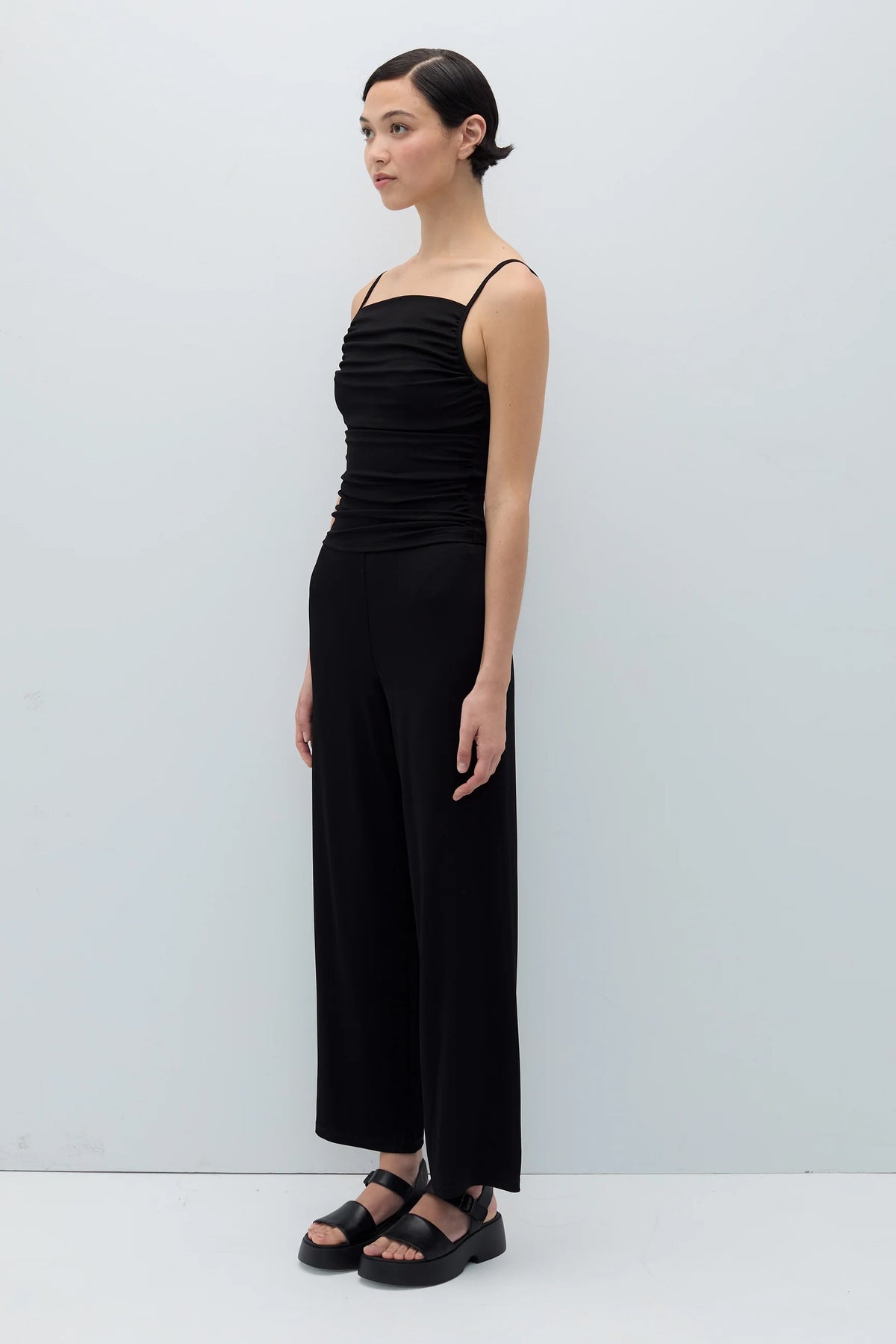 Woman wearing a black ruched top and wide-leg pants against a white background