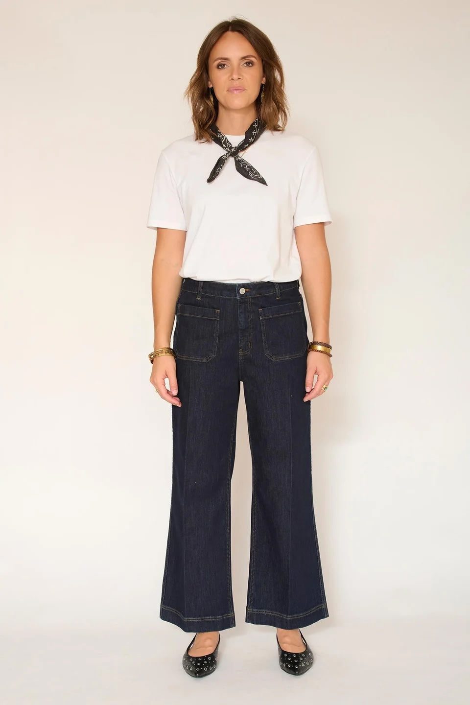 Person wearing a white t-shirt with a black scarf, dark blue jeans, and black shoes on a white background