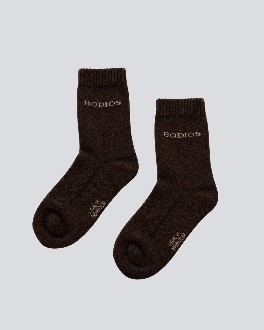 A pair of dark brown crew socks with the brand name  printed in beige near the cuff, displayed on a light gray background.