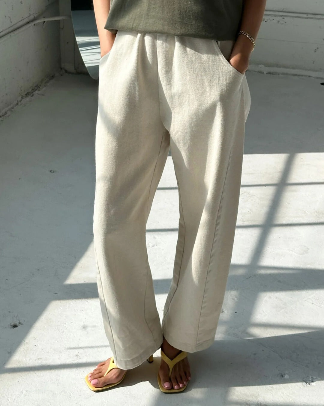 Naturel cream Arc Pants, front view with hands in pockets, styled with an olive top and yellow sandals.