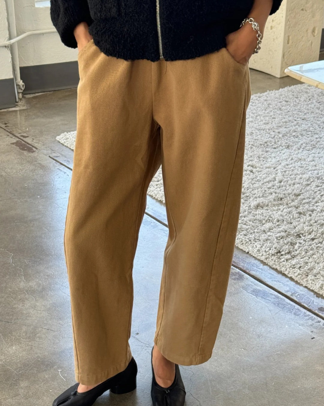 Tobacco brown Arc Pants, front view with hands in pockets, worn with a black jacket and black heeled shoes