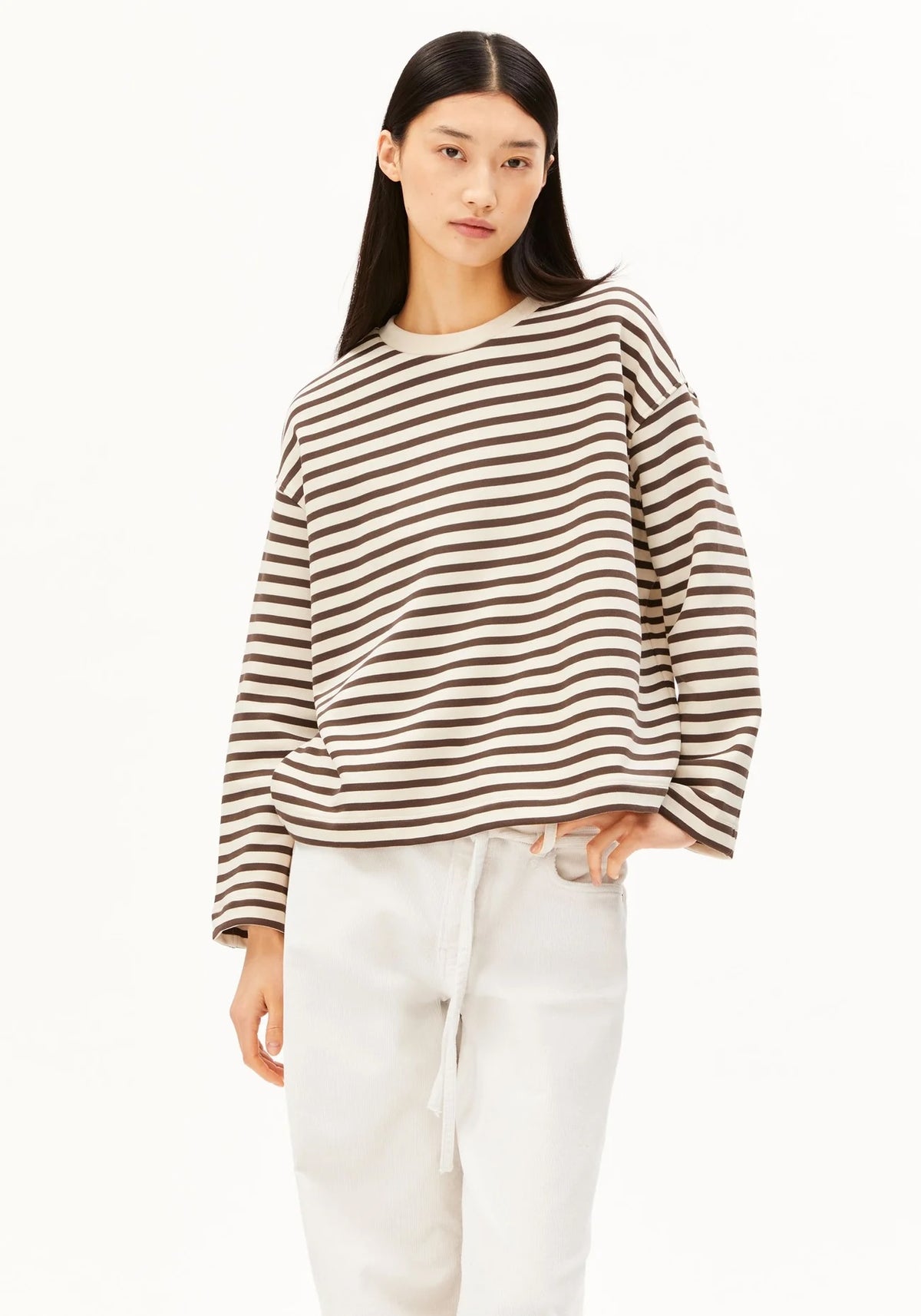A woman modeling a brown and beige horizontally striped long-sleeve knit top with white drawstring pants, shot against a plain white studio background.