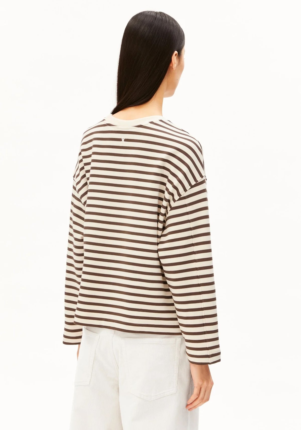 A woman shown from the back wearing a brown and cream horizontal striped long-sleeve top and white pants, against a plain white studio background.