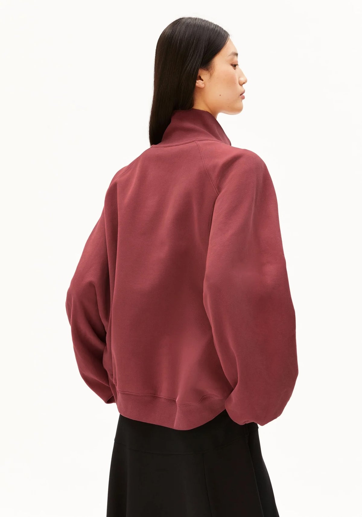 A woman shown from the back wearing a muted burgundy bomber-style jacket with a high mock neck and black bottoms, photographed against a clean white studio background.