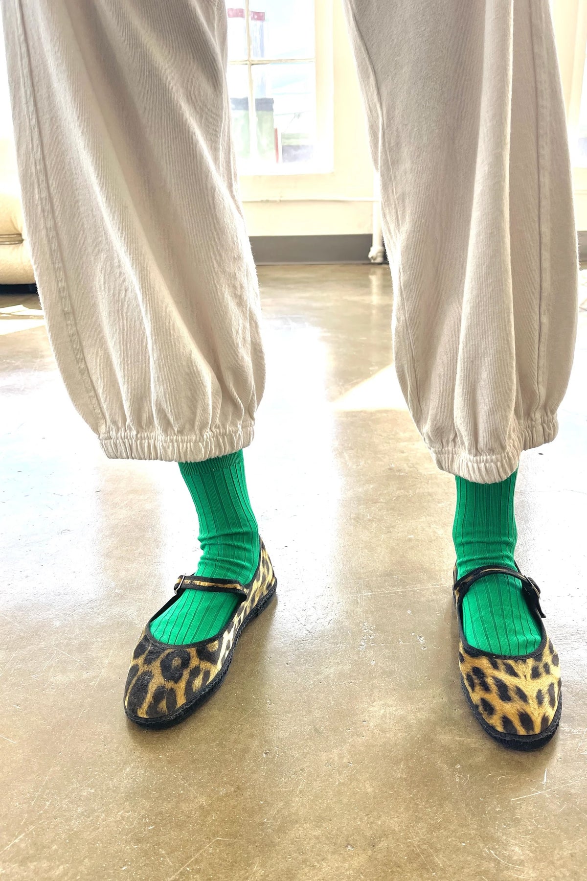 Person wearing leopard print shoes and green socks on a light wooden floor.