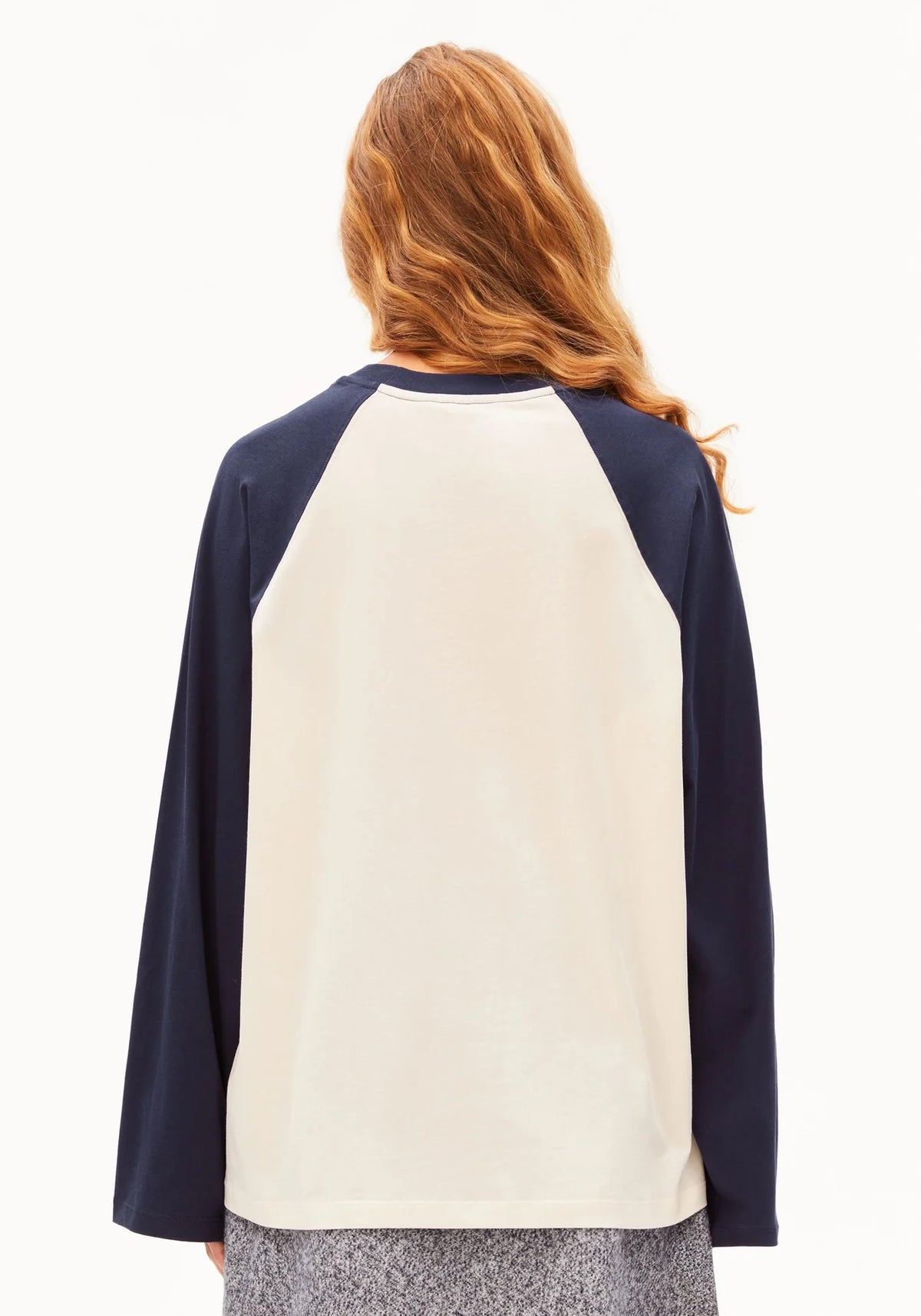 A woman viewed from the back wearing a raglan-style long-sleeve top with a large cream back panel and dark navy sleeves and collar, against a plain white studio background.