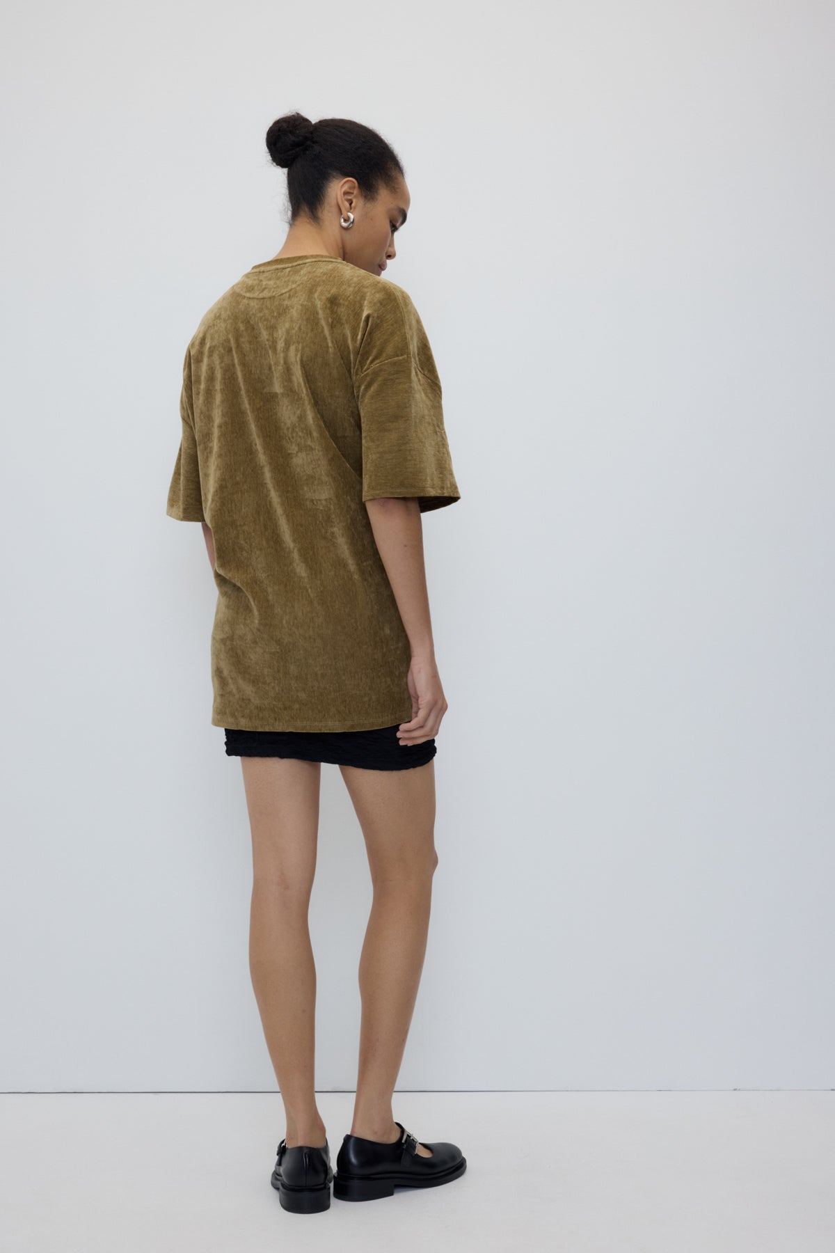 Person wearing a green oversized t-shirt and black shorts against a white background